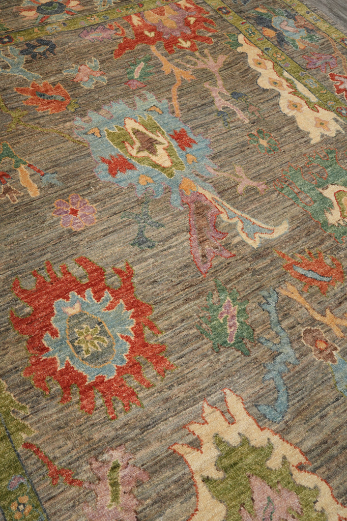 A close-up of a traditional hand-knotted area rug with a textured gray-brown base and intricate floral motifs in red, light blue, green, pink, and beige.