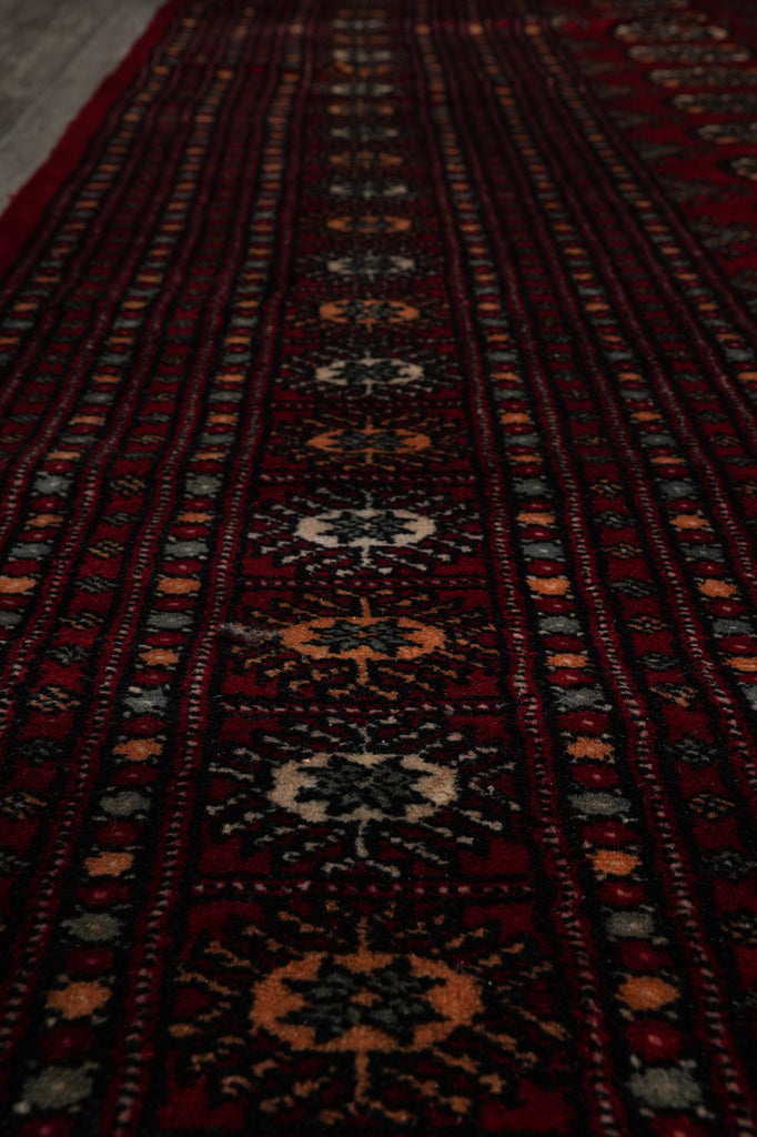 A close-up view of a dark red patterned rug with geometric and floral motifs in black, beige, and orange.