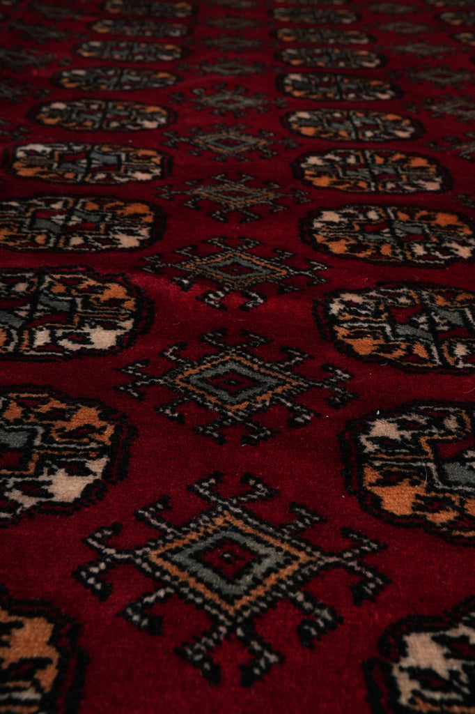 A close-up view of a red patterned rug with traditional geometric medallions and diamond motifs in black, gray, and beige.