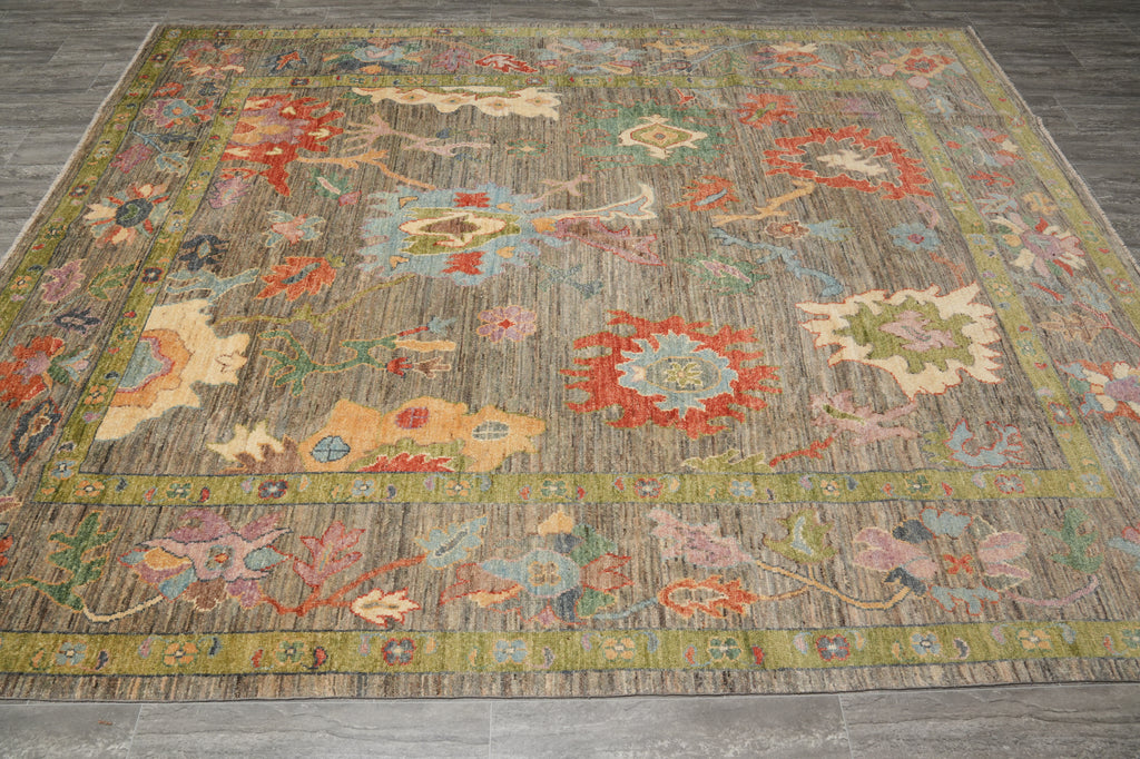 A rectangular area rug with a distressed, vintage-style floral pattern in muted earthy tones of brown, beige, olive green, and red, laid out on a gray tiled floor.