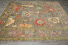 Load image into Gallery viewer, A rectangular area rug with a distressed, vintage-style floral pattern in muted earthy tones of brown, beige, olive green, and red, laid out on a gray tiled floor.