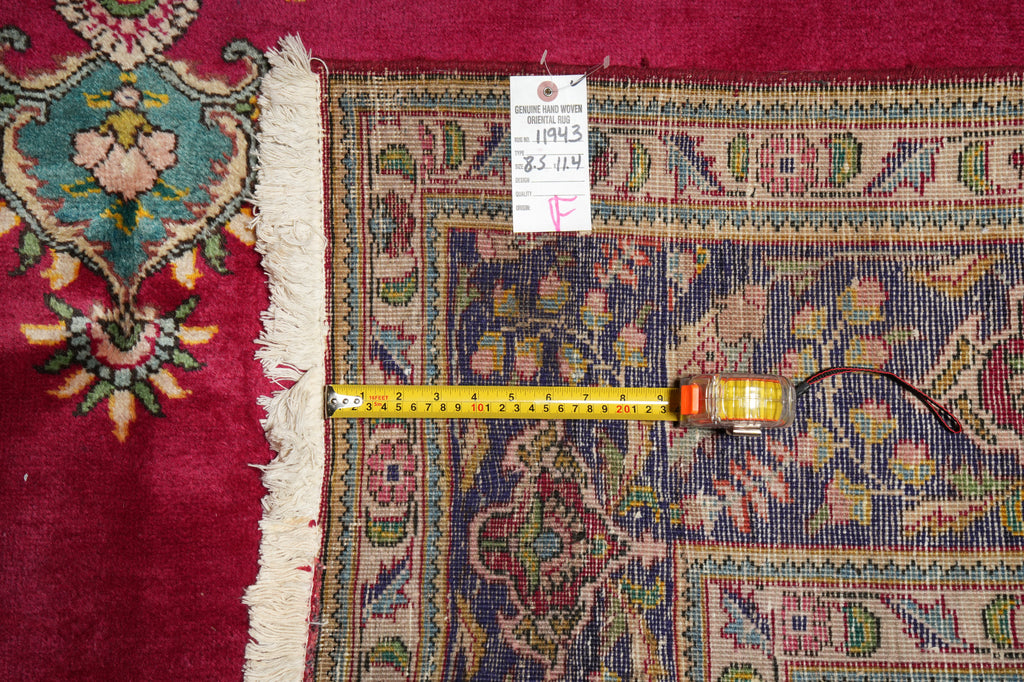 An ornate patterned area rug with cream fringe, shown with a yellow tape measure and a white inventory tag.