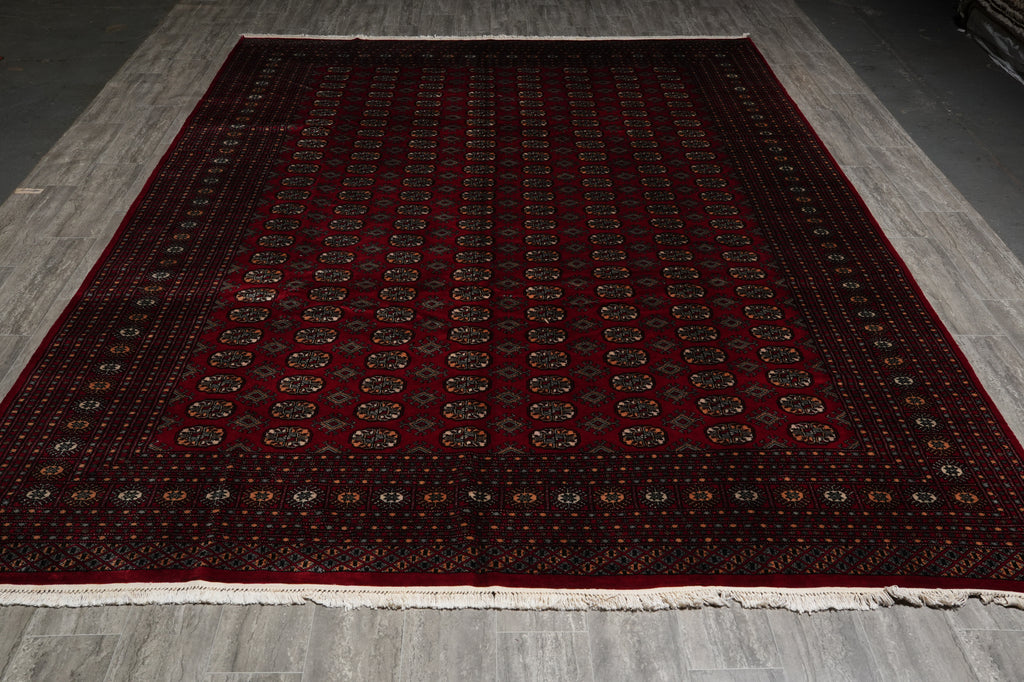 A large rectangular area rug with a deep red field, intricate geometric patterns, and a dark border, laid out on a gray wood-look floor.