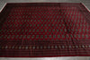 Load image into Gallery viewer, A large traditional Persian-style area rug with a deep red field, featuring rows of small geometric medallions and a detailed patterned border, laid flat on a gray floor.