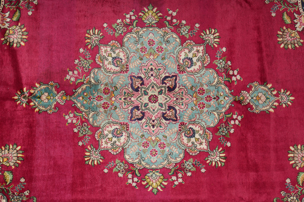 A close-up of a traditional patterned rug featuring a large central medallion in light blue, pink, and green, surrounded by a rich magenta-pink field with floral motifs.