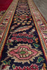 Load image into Gallery viewer, A close-up view of a traditional patterned area rug runner with a dark navy blue center, featuring intricate floral and bird motifs in pink, red, green, and beige, bordered by red and cream patterns.