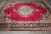 Load image into Gallery viewer, A traditional oriental area rug with a vibrant red field, a central floral medallion, and an ornate navy blue border with floral motifs, laid out on a gray tiled floor.