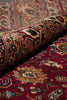 Load image into Gallery viewer, A close-up of a rolled section of a traditional patterned rug resting on another matching rug. The rug features an intricate floral and geometric design in deep red, beige, brown, and muted blue tones.