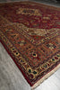 Load image into Gallery viewer, A traditional oriental area rug with an intricate floral and geometric pattern, shown laid out on a gray tiled floor. The rug features a deep red field, a warm beige and brown border, and cream fringe.