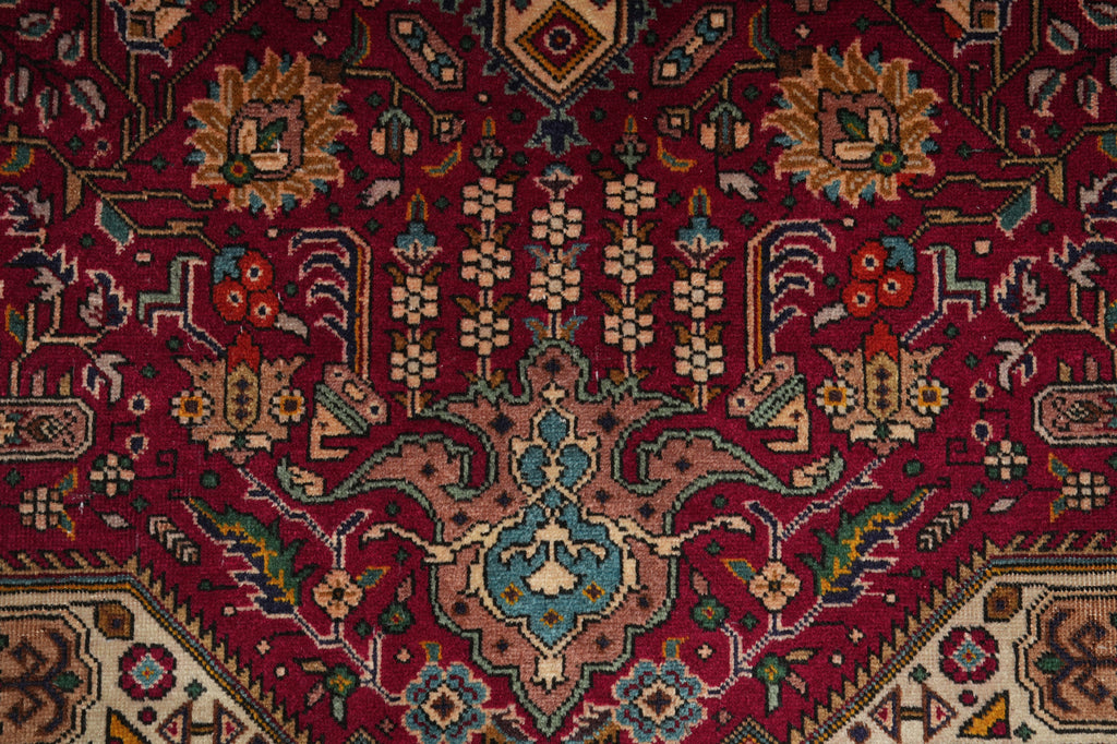 A close-up of a traditional Persian-style area rug with a deep red field, featuring a central medallion and intricate floral motifs in beige, blue, green, and brown.