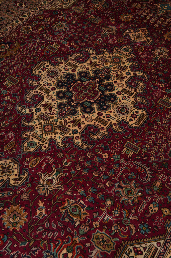 A close-up view of an intricate Persian-style area rug with a deep red field, a large beige central medallion, and detailed floral motifs in black, green, and blue.