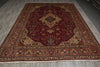 Load image into Gallery viewer, A large traditional Persian-style area rug with a deep red central field, ornate beige and gold borders, and small blue and green accents, laid out on a gray wood floor.