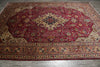 Load image into Gallery viewer, A large traditional Persian-style area rug with a deep red central field, intricate floral motifs, and detailed borders in beige, brown, blue, and green, laid out on a gray tiled floor.