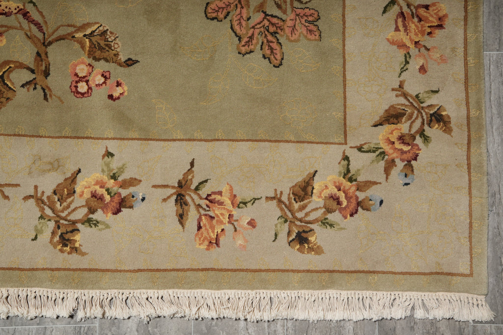 A close-up of a traditional patterned rug with cream fringe, featuring floral motifs in muted peach, brown, and green on a beige background.