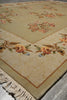 Load image into Gallery viewer, A close-up of a beige area rug with a traditional floral pattern in muted orange, pink, and green tones, featuring a cream-colored fringed edge.