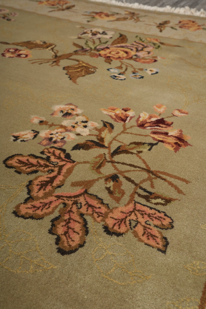 Close-up of a woven textile or rug with a floral pattern in muted peach, brown, cream, and black on a warm beige background.