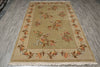 Load image into Gallery viewer, A rectangular area rug with a beige and ochre center field, featuring a floral border and small bird motifs, laid out on a gray wood-look floor.
