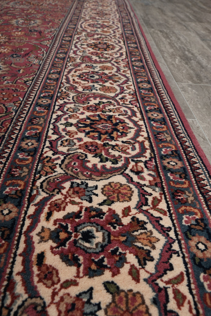 A close-up view of a traditional oriental rug with an intricate floral and medallion pattern in red, beige, navy, and brown, laid out on a gray floor.