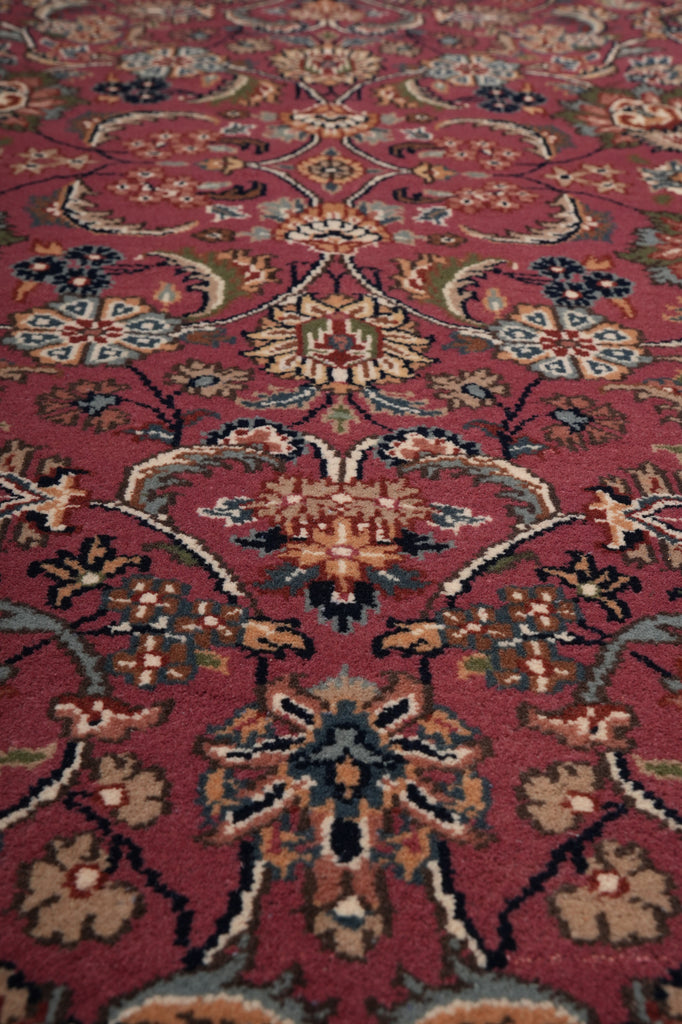 A close-up of a traditional patterned rug with a deep red background and intricate floral motifs in beige, blue, green, and brown.