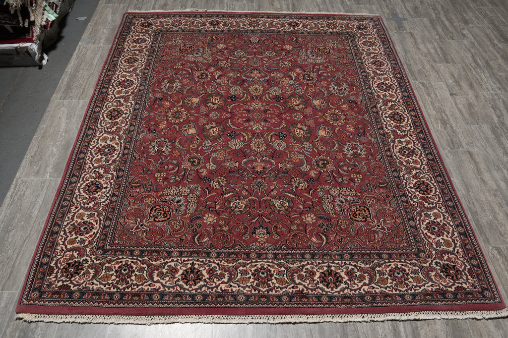 A traditional oriental area rug with a deep red field, ornate floral motifs, and a detailed multi-colored border, laid out on a gray wood-look floor.