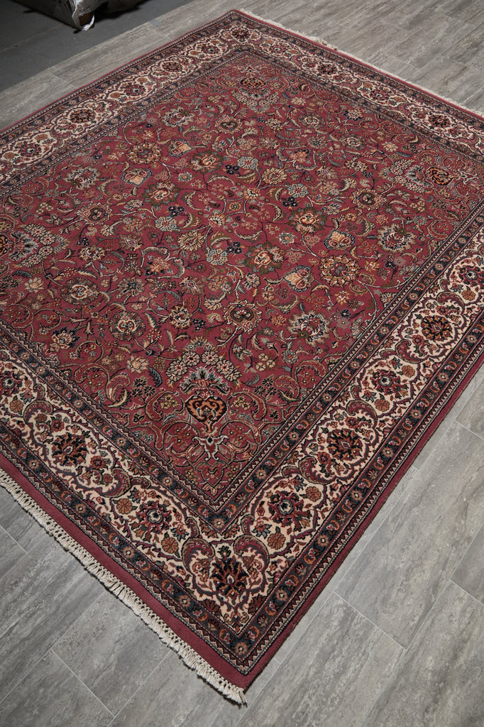 A traditional oriental area rug with a deep red field, intricate floral motifs, and a detailed border, shown laid out on a gray wood-look floor.