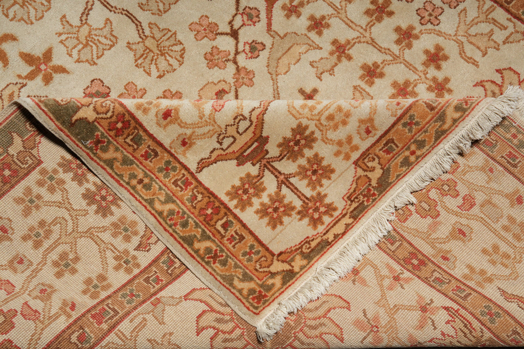 A close-up of a folded area rug with a traditional floral pattern in beige, rust orange, and brown tones, showing the woven texture and fringed edges.