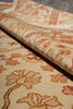 Load image into Gallery viewer, A close-up of a patterned area rug with a rolled section showing its texture and fringe, in warm beige, rust orange, and brown tones.