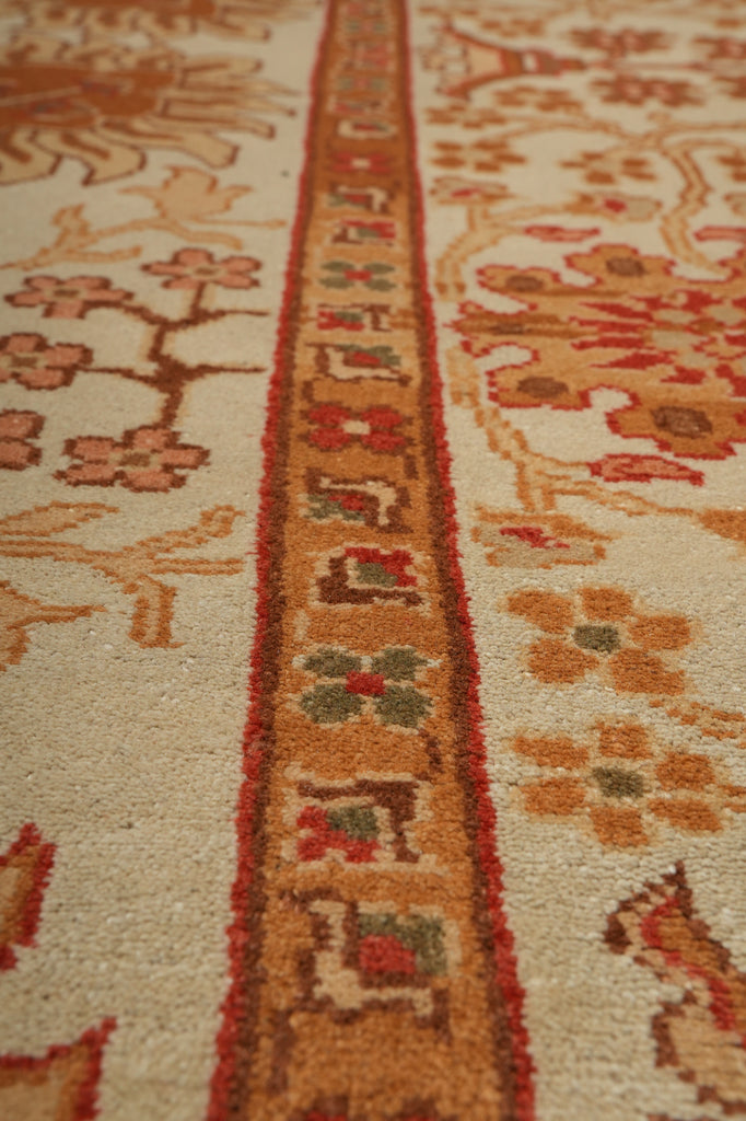 Close-up of a traditional patterned area rug with a central ornate border in rust, red, and green on an off-white background with floral motifs.