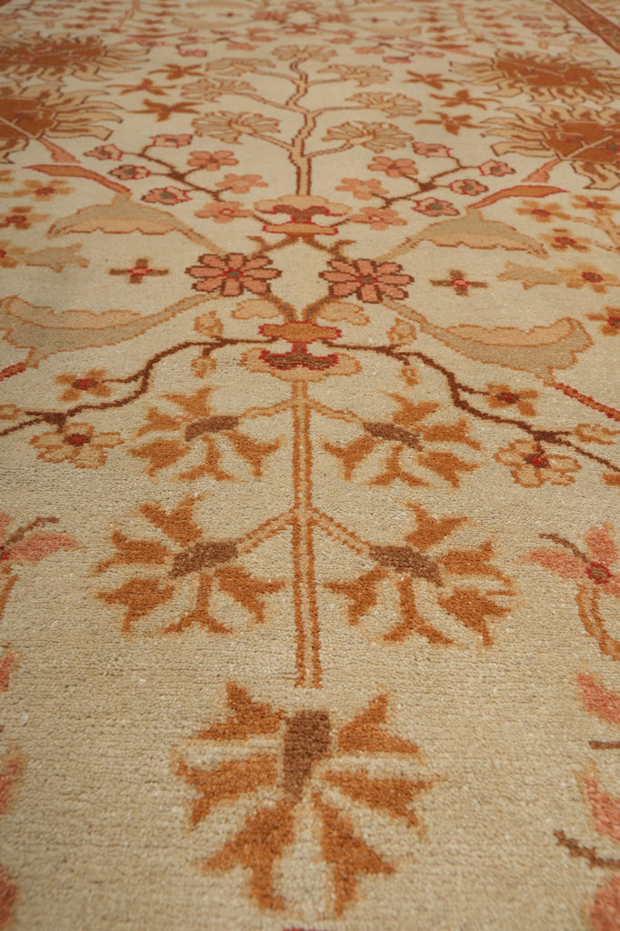 A close-up of a traditional patterned area rug with a warm cream background and floral motifs in rust orange, terracotta, and brown.