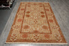 Load image into Gallery viewer, A rectangular area rug with an intricate floral and geometric pattern in beige, rust red, and orange tones, laid out on a gray wood-plank floor.