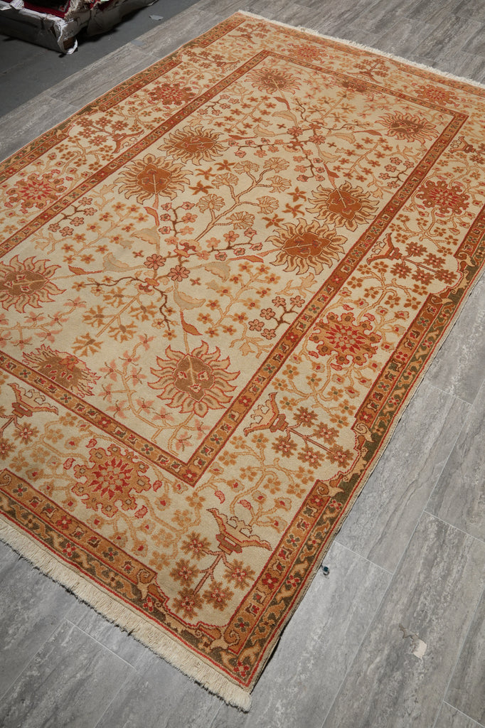 A rectangular area rug with a traditional floral pattern in beige, rust orange, and brown, laid out on a gray wood-look floor.