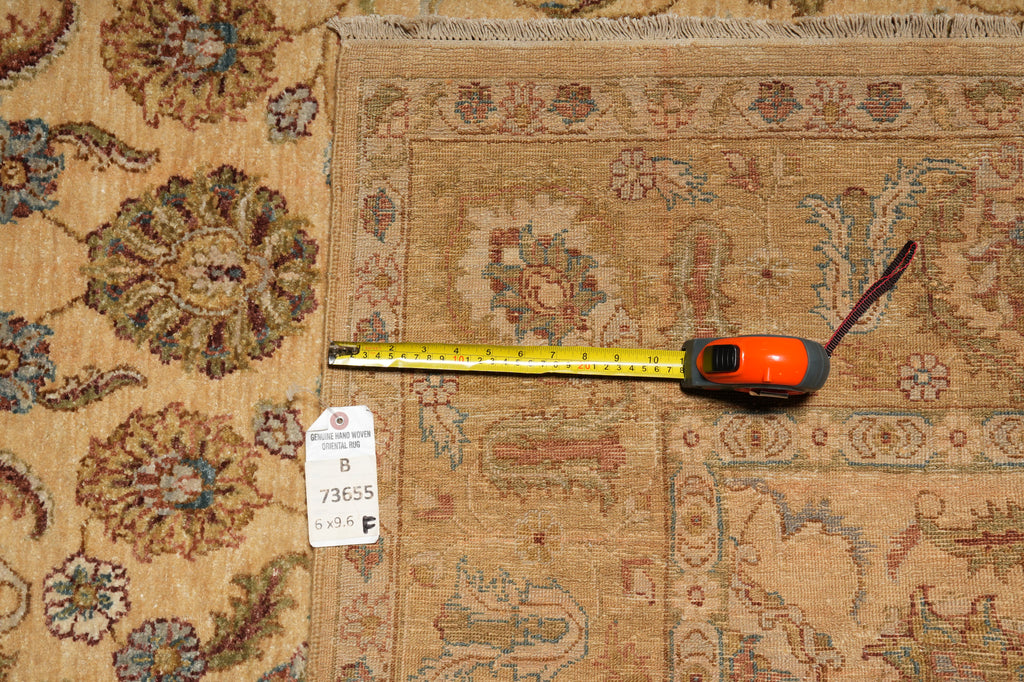 A square patterned area rug in beige and brown tones with floral motifs, shown with a yellow tape measure and a white size tag on top.