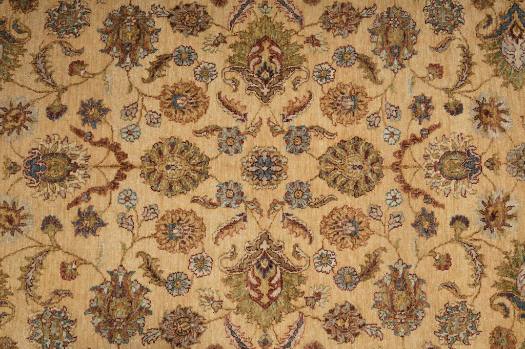 A close-up of an ornate patterned rug or textile with a warm beige background and repeating floral motifs in muted blue, brown, olive green, and rust tones.