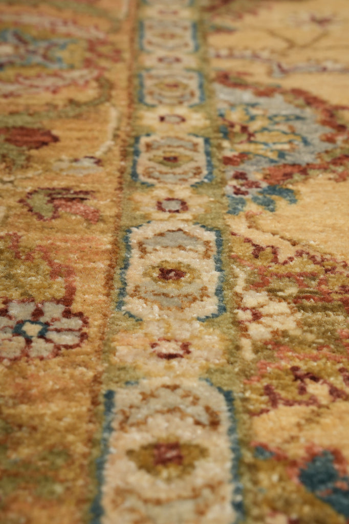 Close-up of a traditional patterned rug with a warm beige and gold base, featuring blue, red, and cream floral motifs.