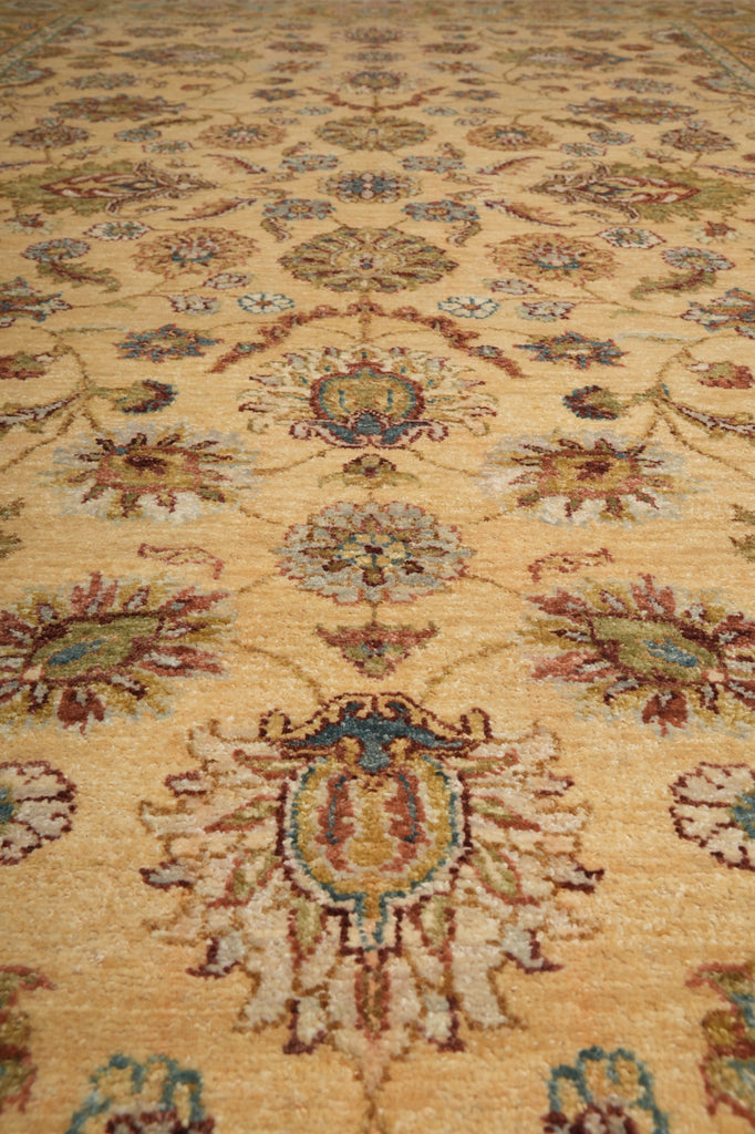 A close-up of a traditional patterned rug with a warm beige background and ornate floral motifs in muted blue, brown, and rust tones.