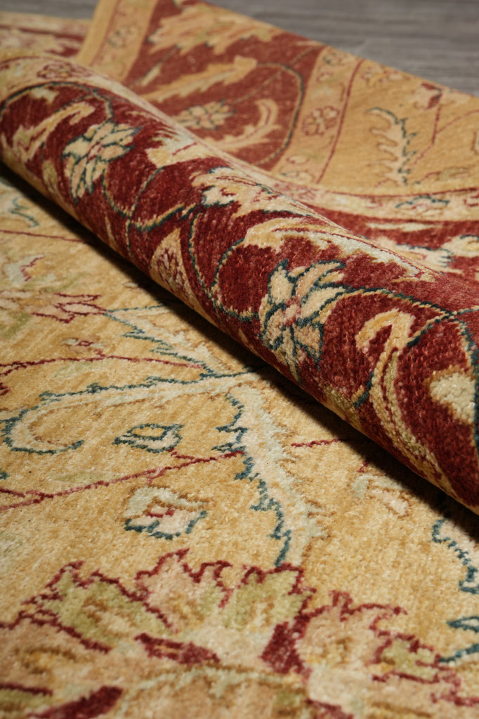 A close-up of a rolled area rug showing its traditional floral pattern in warm beige, rust red, and muted green tones.