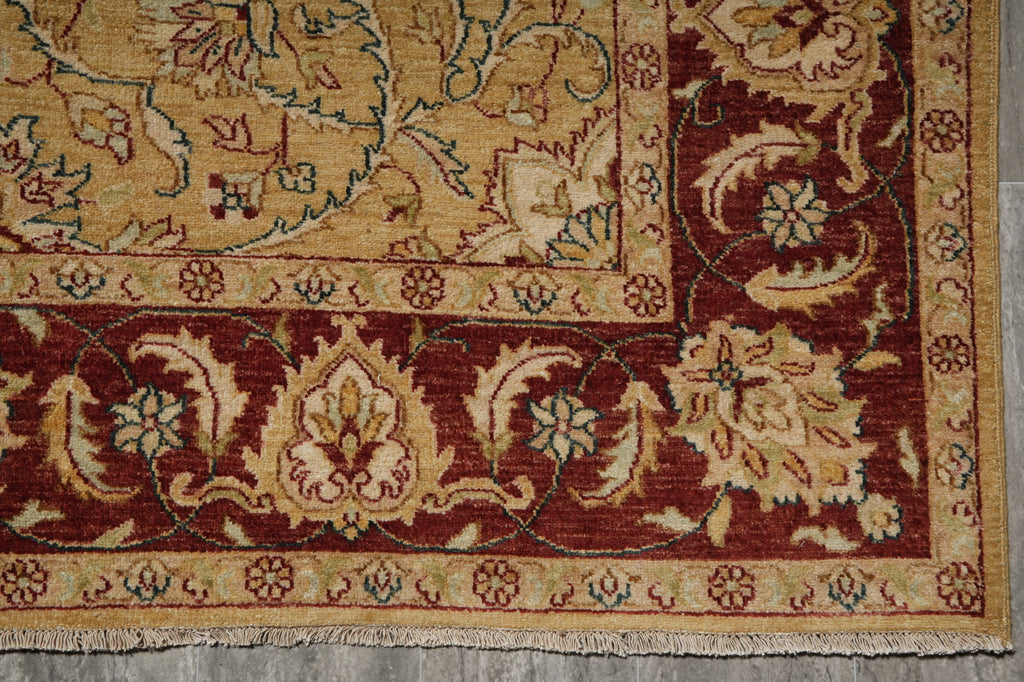 A close-up of an ornate traditional rug corner showing a deep red border with cream and beige floral motifs, a central beige field, and a patterned inner border.