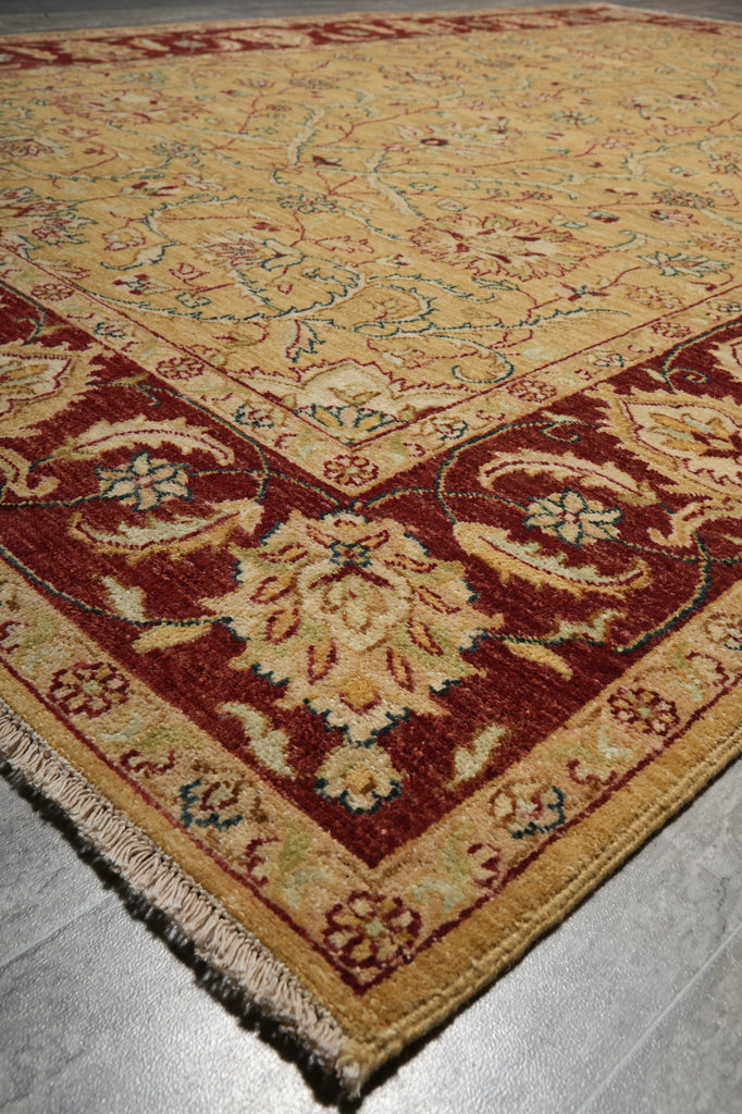 A traditional oriental-style area rug with a beige and red pattern, shown folded over to display its texture and fringe on a gray tiled floor.
