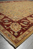 Load image into Gallery viewer, A traditional oriental-style area rug with a beige and red pattern, shown folded over to display its texture and fringe on a gray tiled floor.