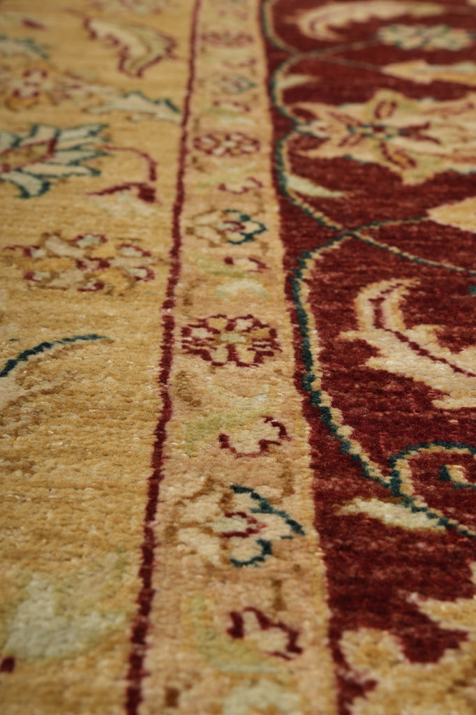 Close-up of a patterned rug with a warm beige background, a dark red border, and cream floral motifs with small teal accents.