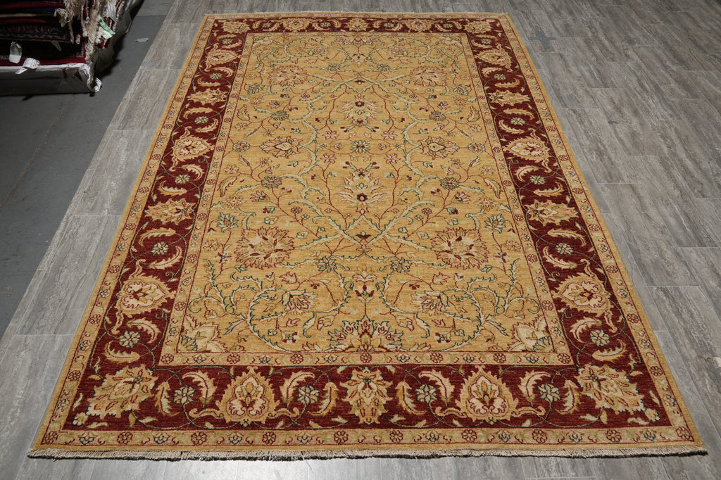 A rectangular traditional area rug with an ornate floral pattern, featuring a golden-yellow center field and a deep red border, displayed on a gray wood-look floor.