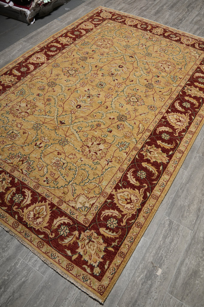 A traditional oriental-style area rug with a beige center field and deep red borders, laid out on a gray tiled floor.