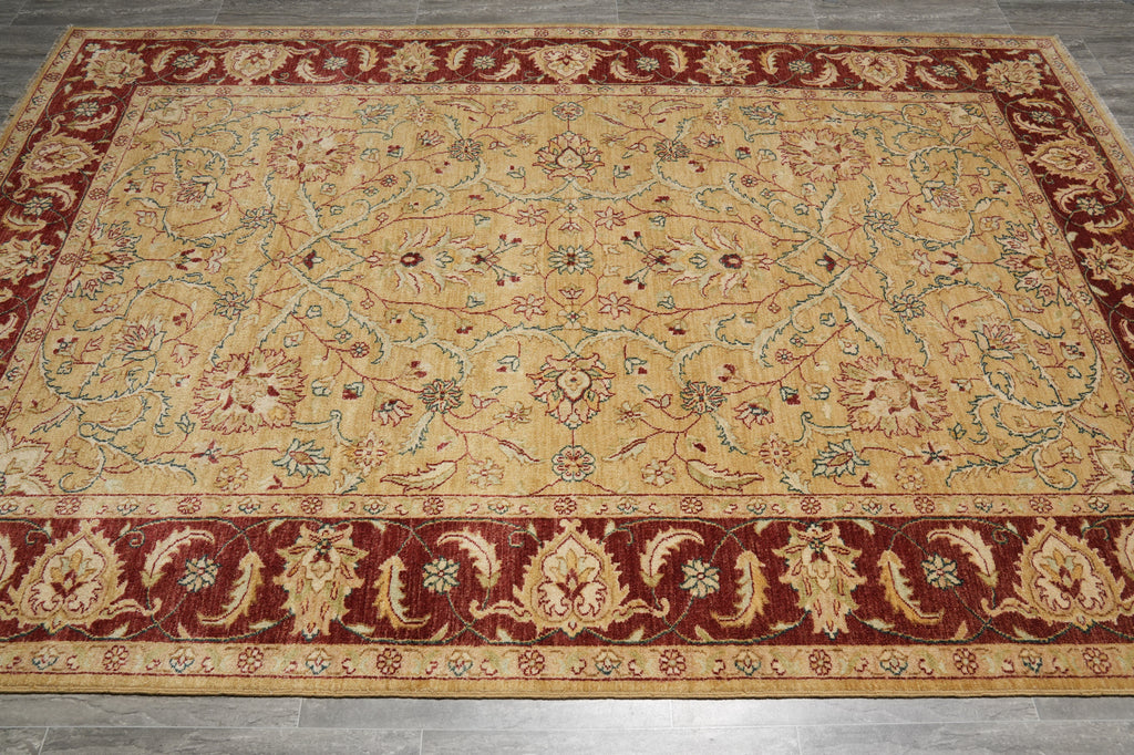 A rectangular area rug with an ornate traditional floral pattern, featuring a beige center field, deep red borders, and accents of green and blue in the detailed motifs.