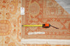 Load image into Gallery viewer, An area rug with a traditional floral pattern in orange, beige, and cream tones, shown with a tape measure and price tag to indicate size and condition.