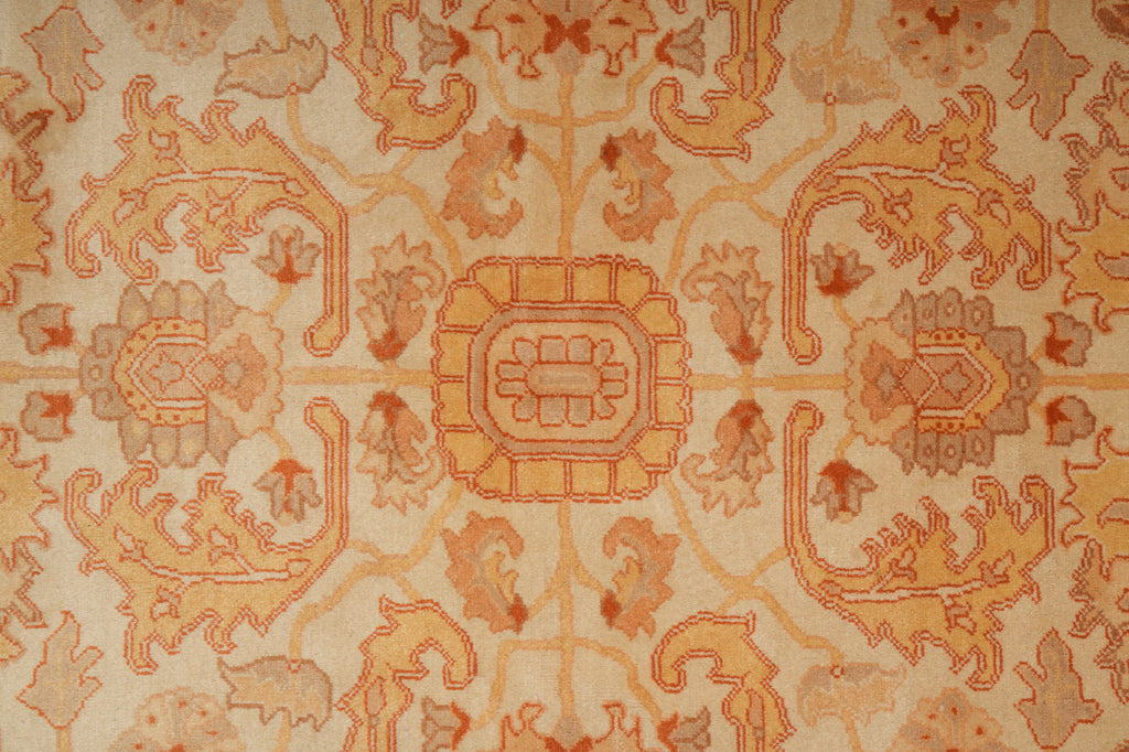 A close-up of an ornate patterned rug or textile with a central medallion and symmetrical floral motifs in warm beige, tan, rust orange, and muted brown tones.