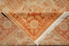 Load image into Gallery viewer, A folded area rug with a warm orange and beige floral pattern, featuring white fringe on one corner, displayed against a matching patterned background.