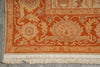 Load image into Gallery viewer, Close-up of an ornate area rug corner showing a warm orange and beige floral medallion pattern with cream fringe at the bottom, laid on a gray floor.