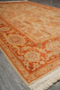 Load image into Gallery viewer, An orange and cream patterned area rug with a traditional floral design and cream fringe, shown laid out on a gray wood floor.