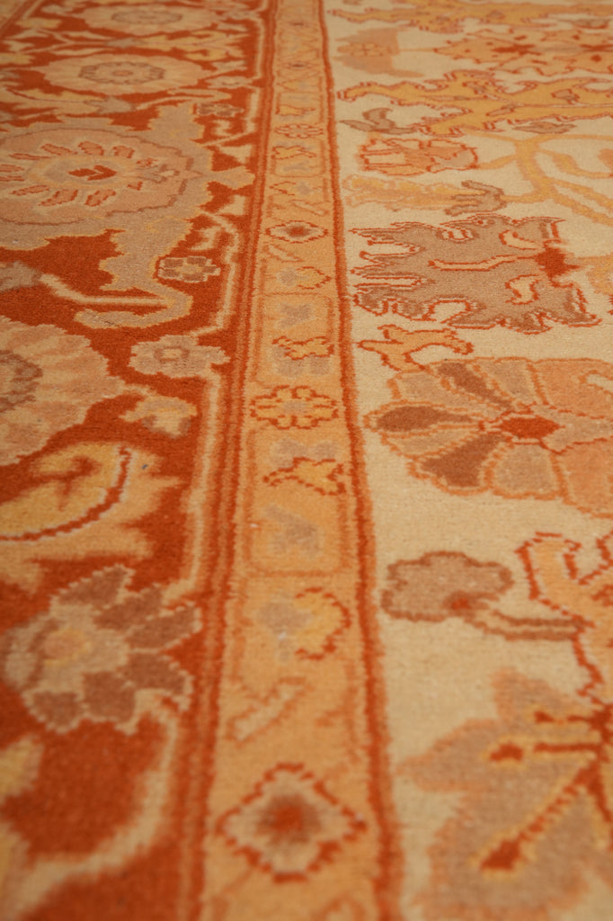 Close-up of a patterned area rug featuring traditional floral and geometric motifs in terracotta orange, beige, and muted brown tones.