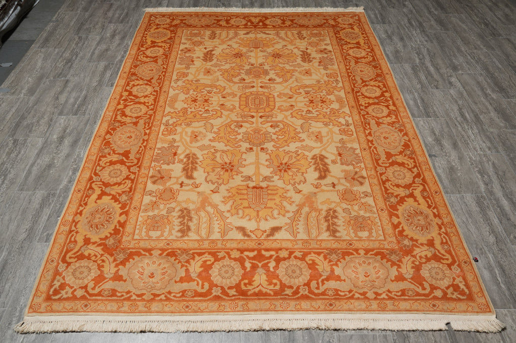 An oriental-style area rug with a traditional floral and medallion pattern, featuring a warm orange border and cream center, laid out on a gray wood-look floor.